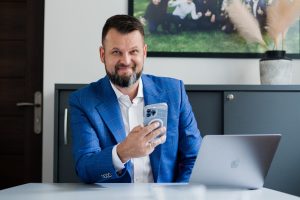 Dzień Bez Telefonu Komórkowego (15 lipca), to święto, które z roku na rok budzi coraz więcej emocji. Może dzieje się tak dlatego, że spełnić oczekiwania tego dnia, czyli zrezygnować z komórki, jest niezwykle trudno. Urządzenie to jest przedłużeniem naszej ręki. Korzystają z niego niestety coraz młodsi. Sprawa jest poważna do tego stopnia, że potrzebne były zmiany w prawie. Smartfon ułatwia nam pracę, życie, ale zabiera też uważność, czas z bliskimi, samodzielność, ma negatywny wpływ na naszą odporność psychiczną. Dlaczego tak ważne jest wprowadzenie cyfrowego detoksu i jak to zrobić? Na początku lipca Sejm uchwalił ustawę, która wprowadza zakaz korzystania z telefonów komórkowych i pokrewnych urządzeń elektronicznych w przedszkolach oraz szkołach podstawowych, a także daje możliwość wprowadzenia zakazu albo określenia innych warunków korzystania z nich w szkołach ponadpodstawowych. Czy nasze społeczeństwo po wielu bardzo głośnych sprawach hejtu i nadużyć zwłaszcza wśród młodzieży a nawet dzieci, zaczynawidzieć zagrożenia wynikające z nadmiernego i niekontrolowanego korzystania z telefonów z Internetem? Z pewnością tak jest. Sama świadomość to bardzo dużo, ale potrzebne są działania oraz budowanie zdrowych nawyków. Takie powinny być kształtowane nie tylko w szkołach, ale przede wszystkim w domach. My mamy telefon… czy telefon ma nas? Tak jak Internetu, również i telefonów z czasem zaczęliśmy używać niezgodnie z ich pierwotnym założeniem. Zamiast rozmawiać z bliskimi, piszemy na grupach na Messengerze. I oczywiście mamy największy problem obecnej ludzkości, czyli bezmyślne, wielogodzinne scrollowanie. Smartfony celowo są projektowane w taki sposób, aby możliwie jak najbardziej zająć nasz czas i skupić na sobie uwagę. Aplikacje mają nas przyciągnąć na jak najdłużej i pokazać nam multum reklam. Nikt już nie chce oglądać długich filmików. Mamy cierpliwość tylko na shortsy. Wszystko to sprawia, że odłożenie telefonu prowadzi do syndromu odstawienia i poczucia straty. To dobitny dowód na to, że jesteśmy wówczas uzależnieni. Nastoletnie dzieci, ale i młodsze, nie potrafią się skupić na nauce i np. czytaniu podręcznika, bo spoglądają na smartfonu i myślami są na Instagramie czy Tik Toku. Ich mózg domaga się dopaminy. To dokładnie tak jak w przypadku narkotyków. Coraz więcej nauczycieli zgłasza, że uczniowie mają wręcz problem z czytaniem wyrazów i nie mówią tu o drugoklasistach, ale starszych dzieciach, które umiejętność czytania powinny mieć opanowaną. Problem staje się coraz bardziej dotkliwy. - Telefon przestał służyć nam, role się odwróciły. Dlaczego? Ponieważ coraz powszechniejsze stają się uzależnienia od telefonu, jego aplikacji i świata, który nam oferuje, niestety często jedynie wirtualnego. Poczucie niepokoju czy wręcz paniki, przymus ciągłego bycia w pobliżu urządzenia czy też niechęć do zostawienia go w innym pokoju, to zaledwie kilka z objawów poważnego uzależnienia behawioralnego, wśród innych o podobnych objawach wymienia się między innymi uzależnienie od alkoholu czy narkotyków. Często już zresztą telefony nazywa się „kokainą naszych czasów” – mówi Jakub B. Bączek, mentor, autor książek i szkoleniowiec. Długotrwałym skutkiem nadużywania smartfonu są stany lękowe czy depresje właśnie przez nieumiejętność odróżnienia prawdziwego życia od tego, co widzimy w social mediach, filmikach, reklamach. Zwłaszcza młodzież nie potrafi zrozumieć, że to, co pokazują ich idole - influencerzy, jest starannie zaplanowaną taktyką. - Najnowszy problem to powszechne już używanie AI i trudność z odróżnianiem tzw. deepfake’ów od rzeczywistego wideo. Treści nawet nieprawdziwe, są bardzo realistyczne. Nabieramy się nawet my, dorośli, a cóż dopiero dzieci, które nie mogą znać czasów przed erą Internetu – dodaje mentor. Międzynarodowy Dzień Bez Telefonu Gdy nie wiesz, gdzie znajduje się twój telefon, przeżywasz mini-zawał? Czas spróbować ograniczyć korzystanie z tej zdobyczy cywilizacji. Higiena cyfrowa to obecnie konieczność, którą wprowadza do swojej codzienności coraz więcej świadomych osób. - Już sam fakt, że taki dzień istnieje w kalendarzu, to sygnał, że widzimy potrzebę zmiany. Oczywiście jeden dzień to za mało, ale to dobry bodziec. Musimy zacząć od siebie, od sprawdzenia naszych nawyków i realnego przyznania się do tego, jak to wygląda z boku, że być może potrzebujemy nowych wzorców, świadomych decyzji, że telefon nie musi nami rządzić. Między innymi na ten temat będę rozmawiał z uczestnikami podczas tegorocznego Roadshow w miastach w całej Polsce. Jak budować odporność psychiczną, której tak bardzo teraz potrzebujemy? W jaki sposób radzić sobie z olbrzymim chaosem i natłokiem informacji? Nie chcę oglądać smutnych obrazków, gdzie do rodziców podchodzi małe dziecko, a oni wybierają telefon, nie poświęcając uwagi temu małemu człowiekowi. Co jest dla nas ważniejsze? Czy na randkach potrafimy jeszcze rozmawiać? Czy tylko gapić się w ekran? Czy jesteśmy w stanie obejrzeć dwuipółgodzinny film bez sięgania po to małe pudełko, aby sprawdzić powiadomienia? To wszystko wymaga dużej samodyscypliny, samoświadomości i treningu, ale jest absolutnie do zrobienia – tłumaczy Jakub B. Bączek. Cyfrowy detoks i sztywne ramy korzystania ze smartfonu są koniecznością Trudno wymagać od dzisiejszego świata, aby zrezygnował z telefonów, jest to niemożliwe. Wiele zawodów nie ma racji bytu bez tego urządzenia. Używanie ich jednak w czasie wolnym powinno odbywać się świadomie i z postawieniem granic. Można zacząć od podstaw, czyli od godz. 21:00 telefon jest w innym pomieszczeniu, nie kładziemy go koło łóżka w sypialni. W restauracji czy podczas spotkań z rodziną i znajomymi smartfony nie powinny leżeć na stole, najlepiej, gdy pozostają schowane w torebce. Do łask wracają nawet tradycyjne aparaty fotograficzne, budziki, zegarki. To znak, że ludzie czują potrzebę odstawienia telefonu i powrotu do analogowych urządzeń. - Jeśli chodzi o dzieci, oprócz ograniczeń w szkołach, podstawą będzie to, co obserwują w domu. Jeżeli rodzice cały czas spędzają oddzielnie z nosem w telefonie, nie rozmawiając ze sobą, nie jedząc wspólnych posiłków, nie oczekujmy od pociech, że będą inaczej się zachowywać. Trzeba wprowadzić jasne zasady i dać młodszemu pokoleniu przykład. Odpowiedzialność jaka obecnie na nas ciąży jest olbrzymia. W krajach skandynawskich coraz częściej rodzice dzieci w klasie umawiają się, że nikt nie dostaje telefonu, aby żadne dziecko nie czuło się wykluczone. Być może jest to jakieś rozwiązanie, które będzie wspierać najmłodszych. Uzależnienie od smartfonu zdarza się już nawet u kilkulatków, co jest zatrważające, bo ktoś im to urządzenie dał o wiele za wcześnie i tym samym zabrał możliwość naturalnego rozwoju mózgu i funkcji poznawczych. Konsekwencją jest długotrwałe leczenie i terapia. Unikajmy tego, technologia jest dobra tylko wtedy, gdy w dobrej wierze z niej korzystamy. Granica jest bardzo cienka i trzeba uważać, aby jej nie przekroczyć. Żadne urządzenie nie zastąpi kontaktu z drugim człowiekiem i wspólnie spędzonego czasu – mówi Jakub B. Bączek. Sięganie po telefon stało się naszym nawykiem, pamięć mięśniowa robi to za nas. Łapiemy się na tym, że oglądając film, nie potrafimy się skupić, bo zaglądamy do telefonu. Trzeba ten proces odwrócić, wylogować się do życia, telefon zostawiać w innym pokoju. Na początku będzie trudno, ale warto konsekwentnie działać w tym kierunku, budować nowe nawyki, abyśmy to my decydowali, kiedy i jak używamy telefonu, nie odwrotnie.   Jakub B. Bączek - Mentor Mistrzów Świata i olimpijczyków, multiprzedsiębiorca, autor ponad 20 książek, sprzedawanych dziś w 17 krajach. Wykładowca studiów MBA na Akademii Leona Koźmińskiego, ekspert telewizyjny, mówca inspiracyjny, regularnie zapraszany do czołowych banków i korporacji. Twórca Akademii Trenerów Mentalnych™ i popularnych projektów szkoleniowych w Polsce i za granicą. Prywatnie pasjonat podróży, gry w golfa, buddyzmu i czytania książek. Uważa, że marzenia się nie spełniają – marzenia się... SPEŁNIA!